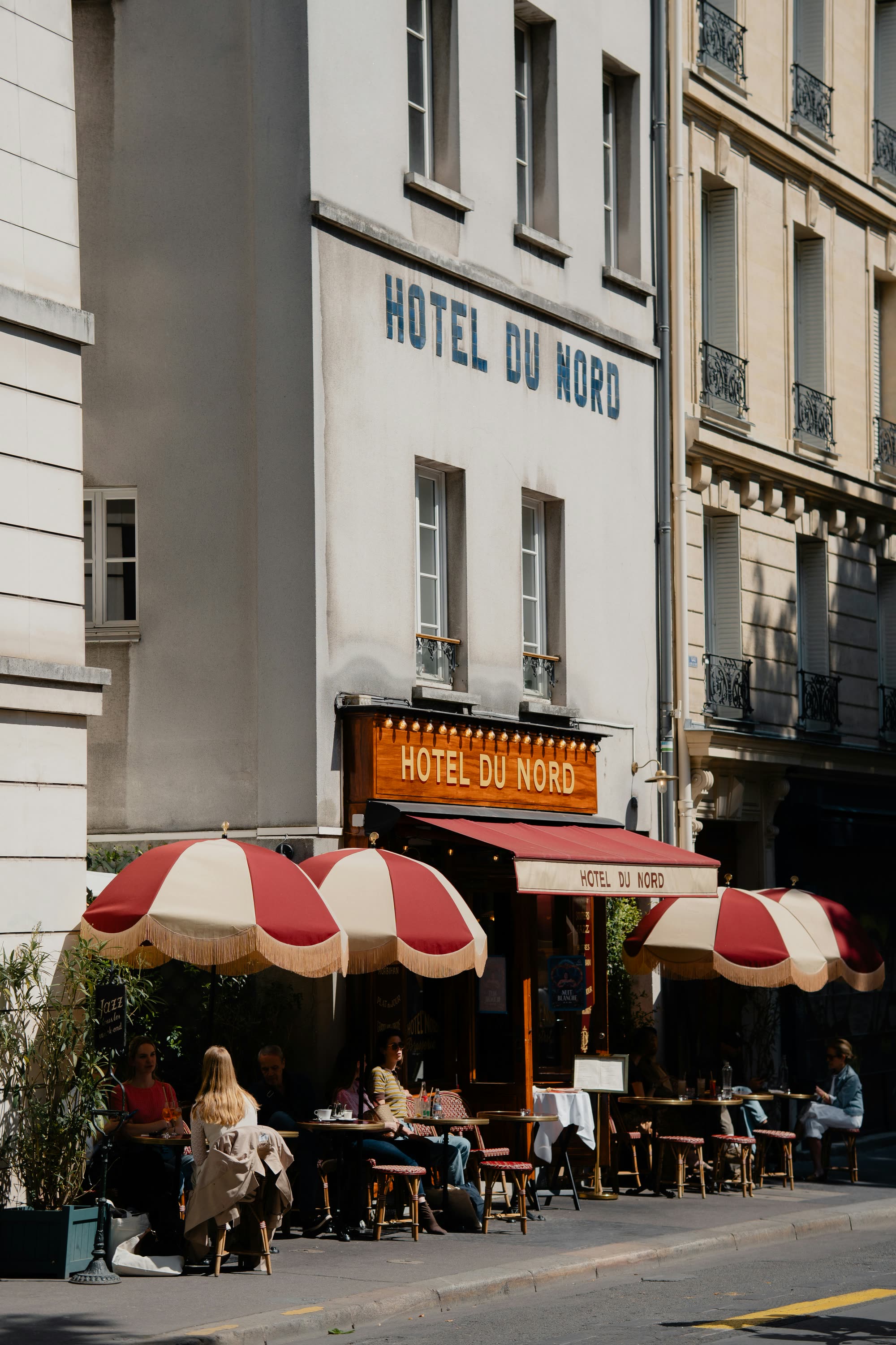 The terrace of Hôtel du Nord, red and cream fringed parasols over café tables on the street