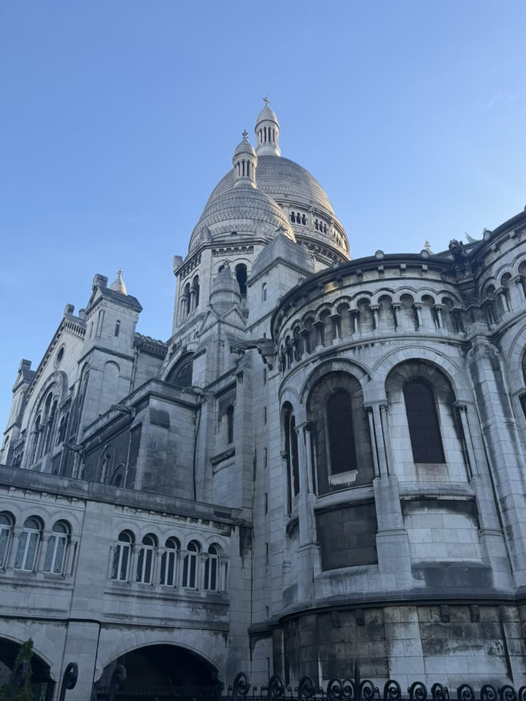 The pale stone apse and dome of Sacré-Cœur against a blue sky
